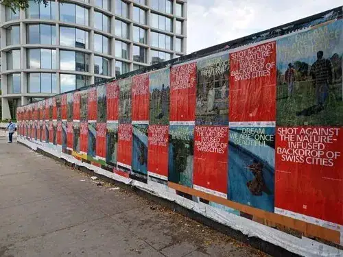 Wall covered with colorful advertising posters promoting Swiss cities, featuring nature-infused imagery and text, showcasing guerrilla marketing techniques for effective brand visibility.