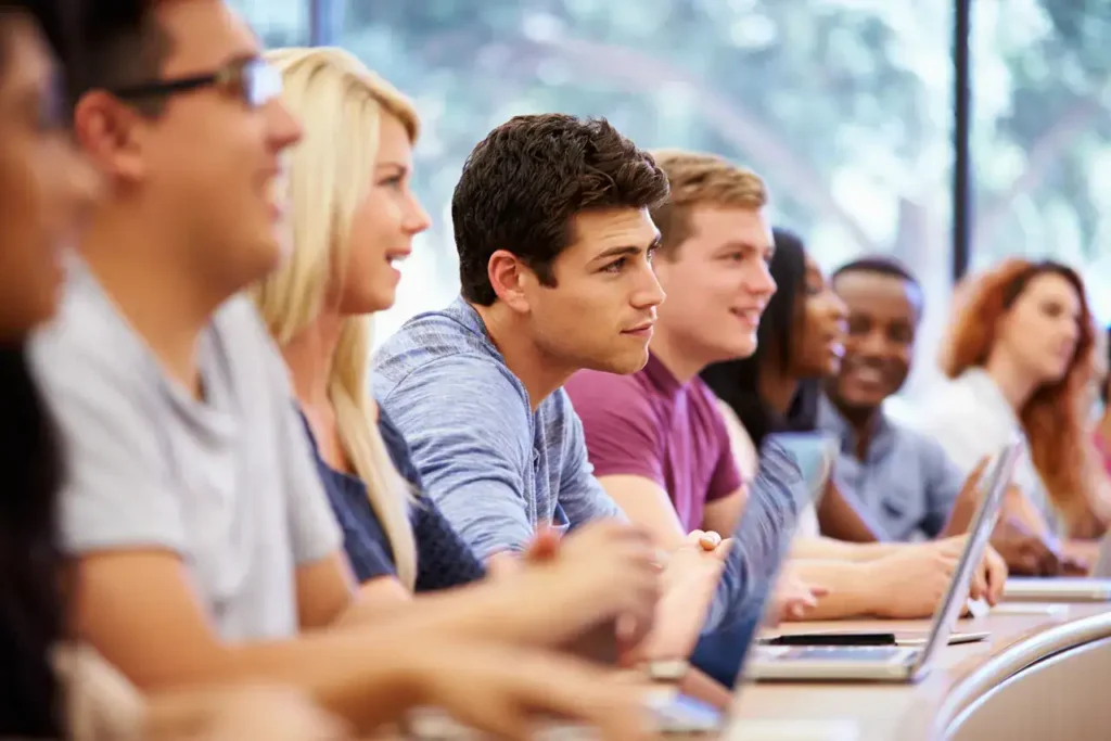 Group of diverse students engaged in a classroom setting, focusing on learning and collaboration, with laptops in front of them, reflecting educational advertising themes.