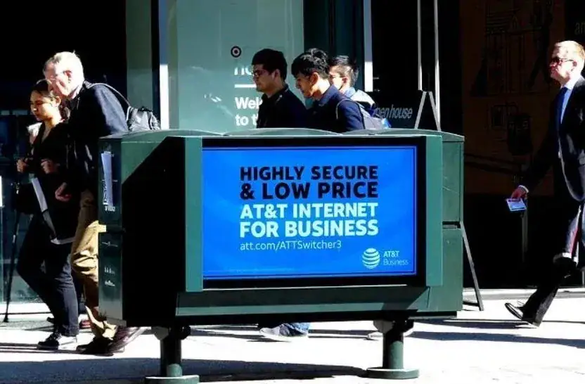 Street furniture advertisement showcasing AT&T Internet for Business, emphasizing "Highly Secure & Low Price," with pedestrians walking by in an urban setting.