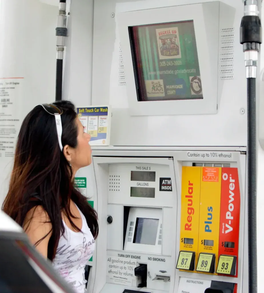 Woman interacting with a gas pump TV screen displaying advertisements, showcasing the effectiveness of gas pump advertising in marketing strategies.