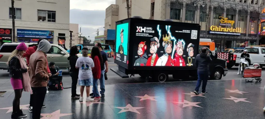 Mobile billboard truck displaying vibrant animated characters in a busy urban setting, attracting attention from a diverse group of pedestrians on Hollywood Boulevard.