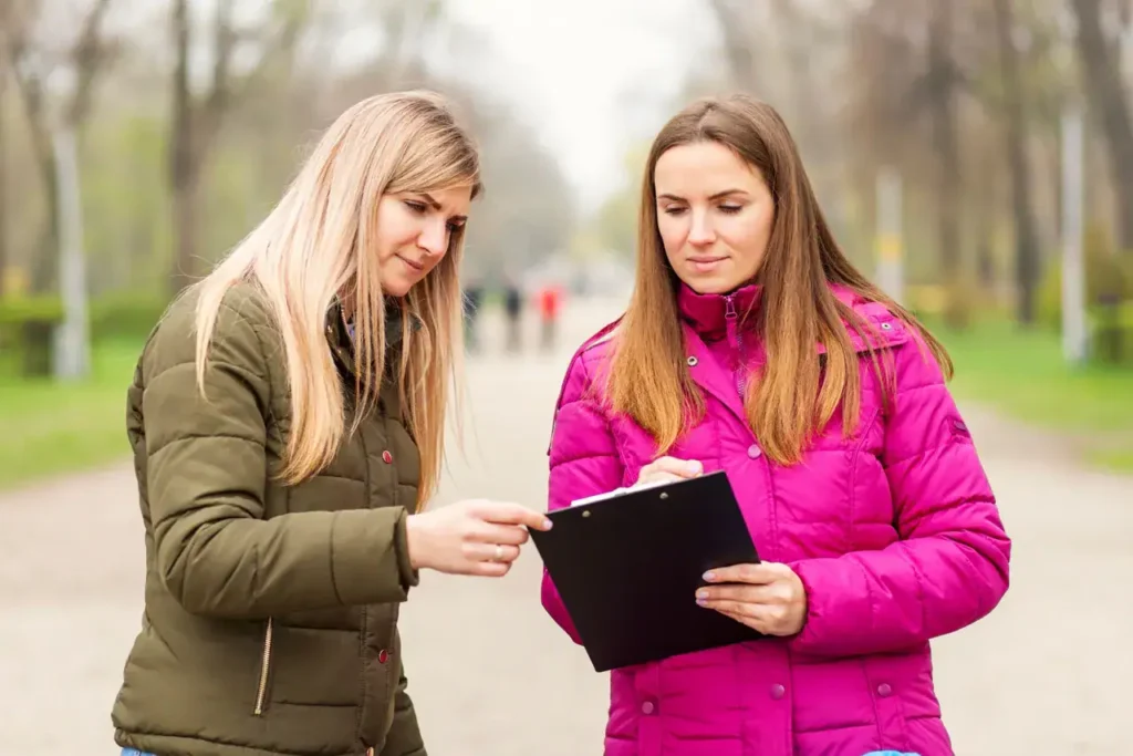 Two women discussing a clipboard in a park setting, highlighting teamwork and collaboration in marketing strategies.