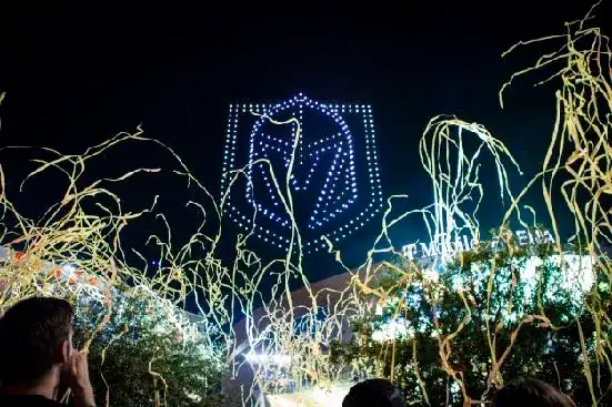 Drone light show featuring illuminated logo display against night sky, surrounded by celebratory streamers, showcasing innovative advertising potential for brands.
