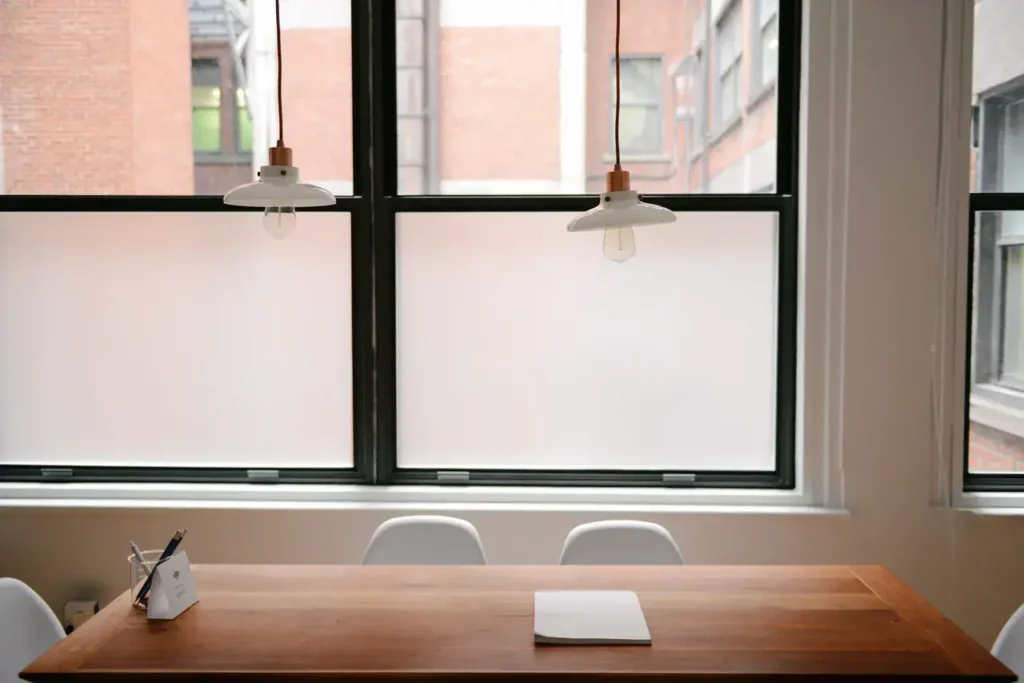 Modern office space with a wooden table, white paper, and pendant lights, featuring large windows with frosted glass in an urban setting, reflecting a professional environment suitable for marketing discussions.
