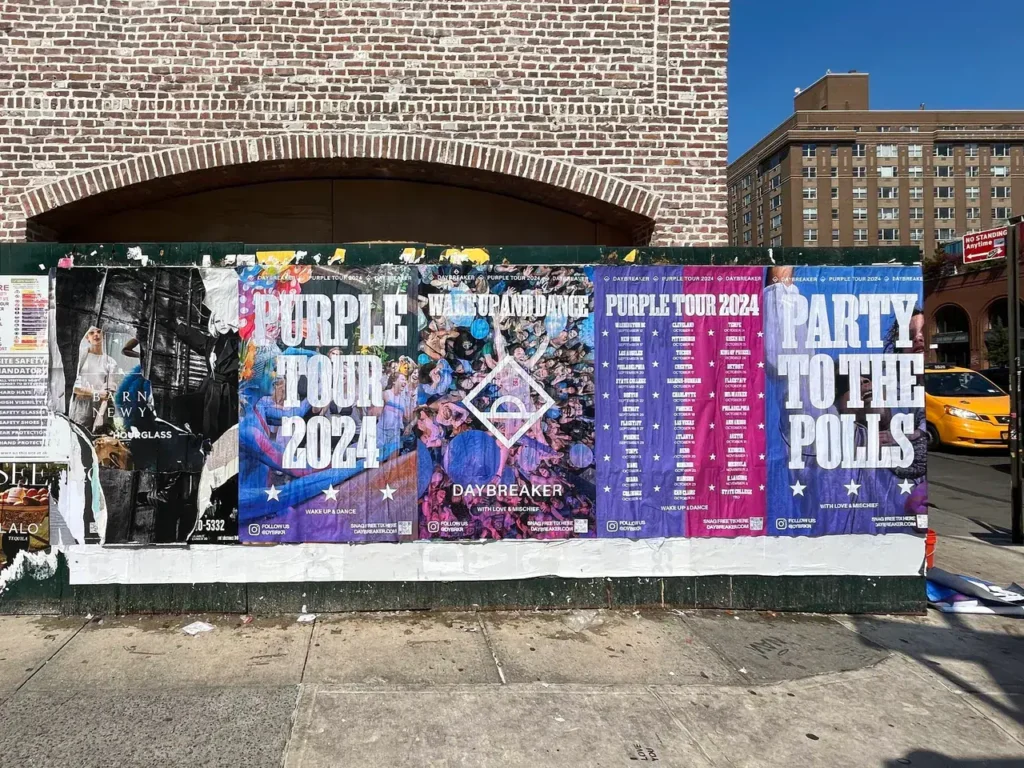 Colorful wall of promotional posters advertising the "Purple Tour 2024," featuring event details and graphics, emphasizing guerrilla marketing strategies for brand visibility.