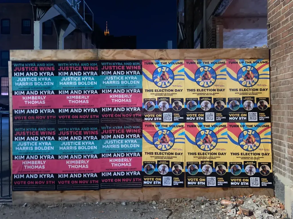Colorful election posters promoting candidates Kim and Kyra, featuring slogans like "Turn Up the Volume" and "Vote on Nov 5th," displayed on a wall in an urban setting, emphasizing guerrilla marketing for political engagement.