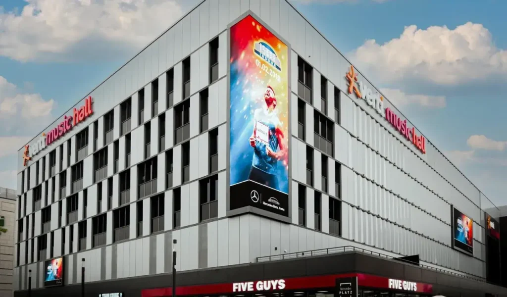 Billboard advertisement on a modern building showcasing a runner with a colorful background, featuring branding for Mercedes-Benz, located near a Five Guys restaurant, emphasizing innovative advertising strategies.