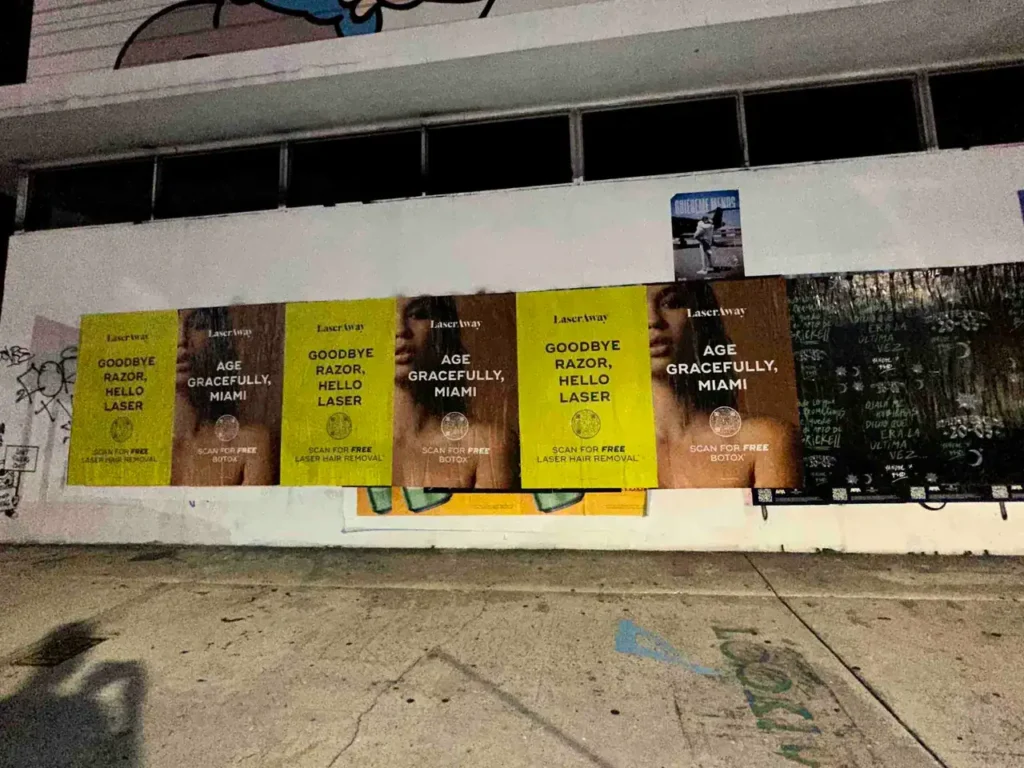 Posters advertising laser hair removal services in Miami, featuring the tagline "Goodbye Razor, Hello Laser" and a call to action for free consultations, set against a graffiti-covered wall.