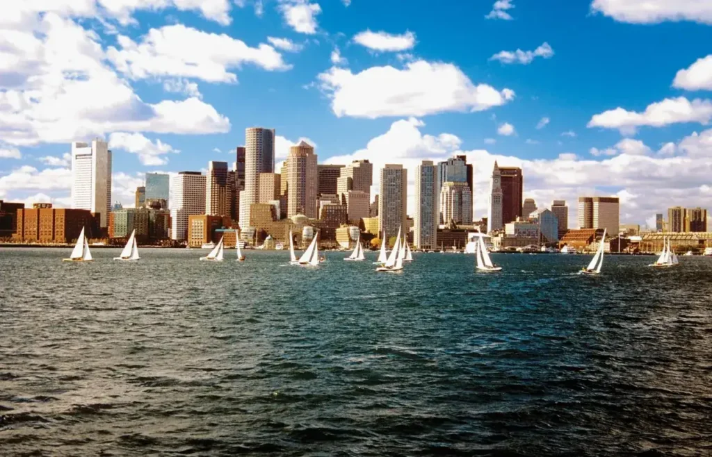 Boston skyline with sailboats on water under a blue sky with clouds, representing outdoor advertising opportunities in urban environments.