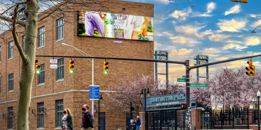 Billboard advertising showcasing cocktails on a building in an urban setting, with pedestrians and traffic lights visible, emphasizing outdoor marketing strategies.