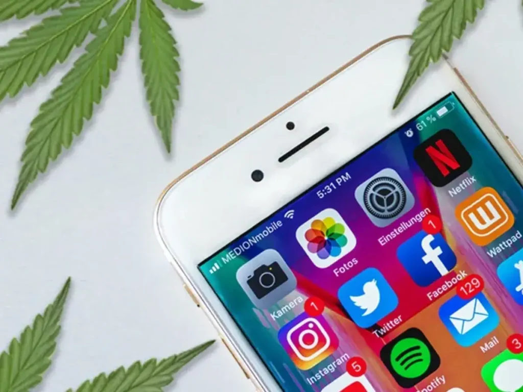 Smartphone displaying social media apps with cannabis leaves in the background, emphasizing marijuana advertising and digital marketing strategies.