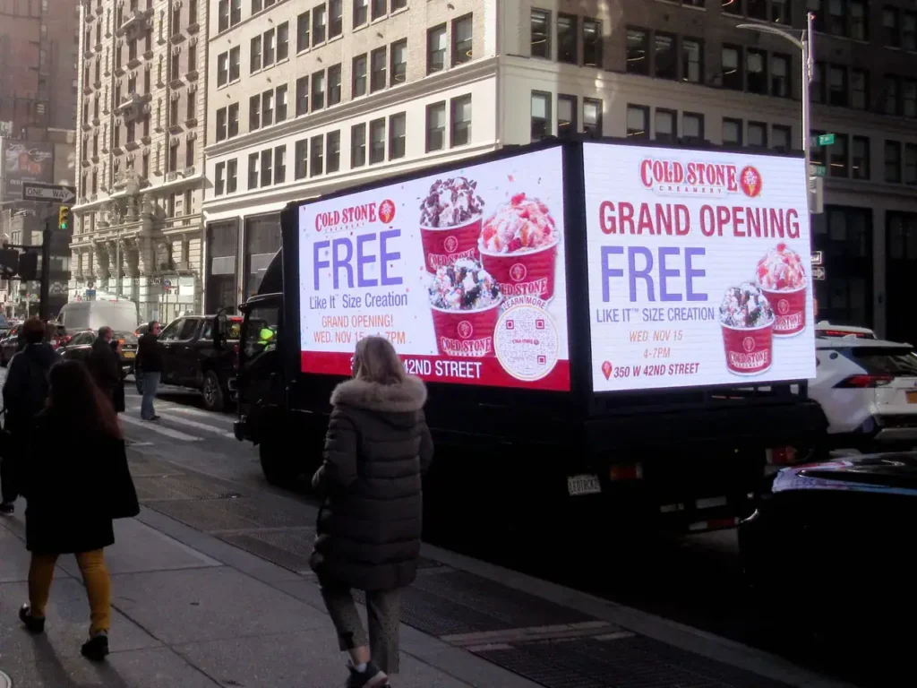 Cold Stone Creamery grand opening advertisement on a mobile billboard, featuring free ice cream promotion, located on 42nd Street in a busy urban setting, with pedestrians walking by.