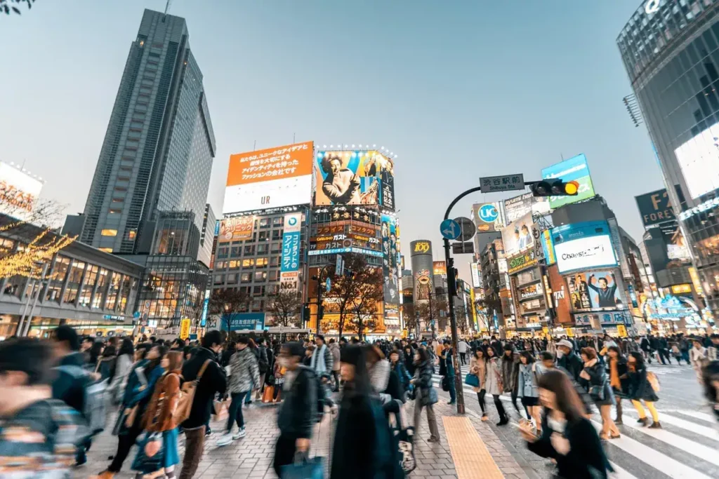 Busy urban intersection in Tokyo, featuring vibrant digital billboards and a diverse crowd of pedestrians, illustrating international advertising and cultural engagement.