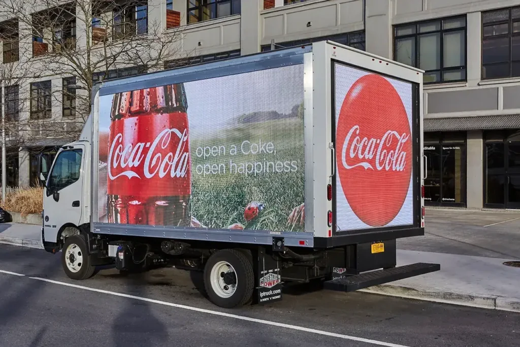 LED billboard truck displaying Coca-Cola advertisement with the slogan "open a Coke, open happiness" in an urban setting.