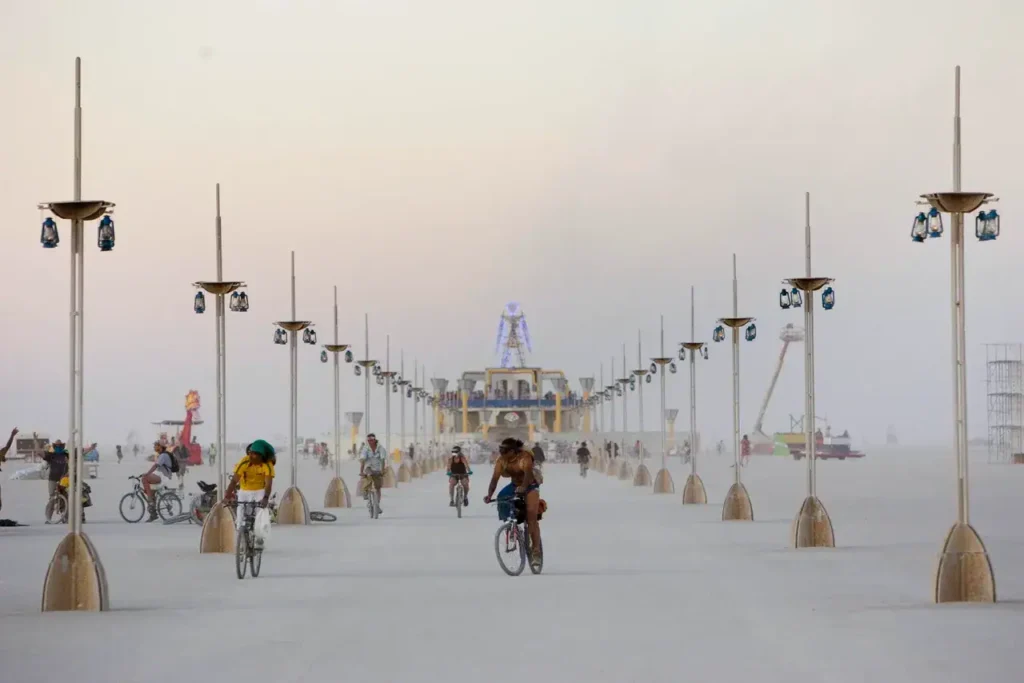Burning Man festival scene with participants biking along a dusty path, illuminated by lanterns, showcasing a vibrant atmosphere for unconventional marketing opportunities.