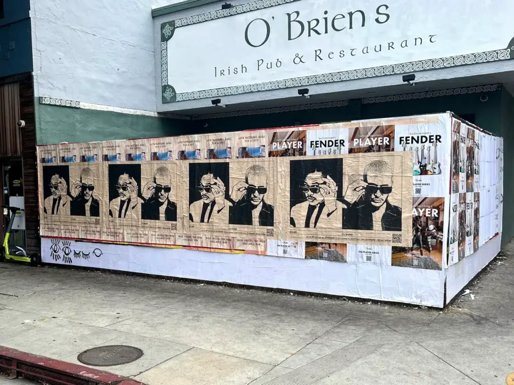 Wheatpaste advertising featuring multiple black-and-white portraits of a stylish figure with sunglasses, displayed on the exterior wall of O'Brien's Irish Pub, surrounded by various promotional posters, illustrating guerrilla marketing techniques.