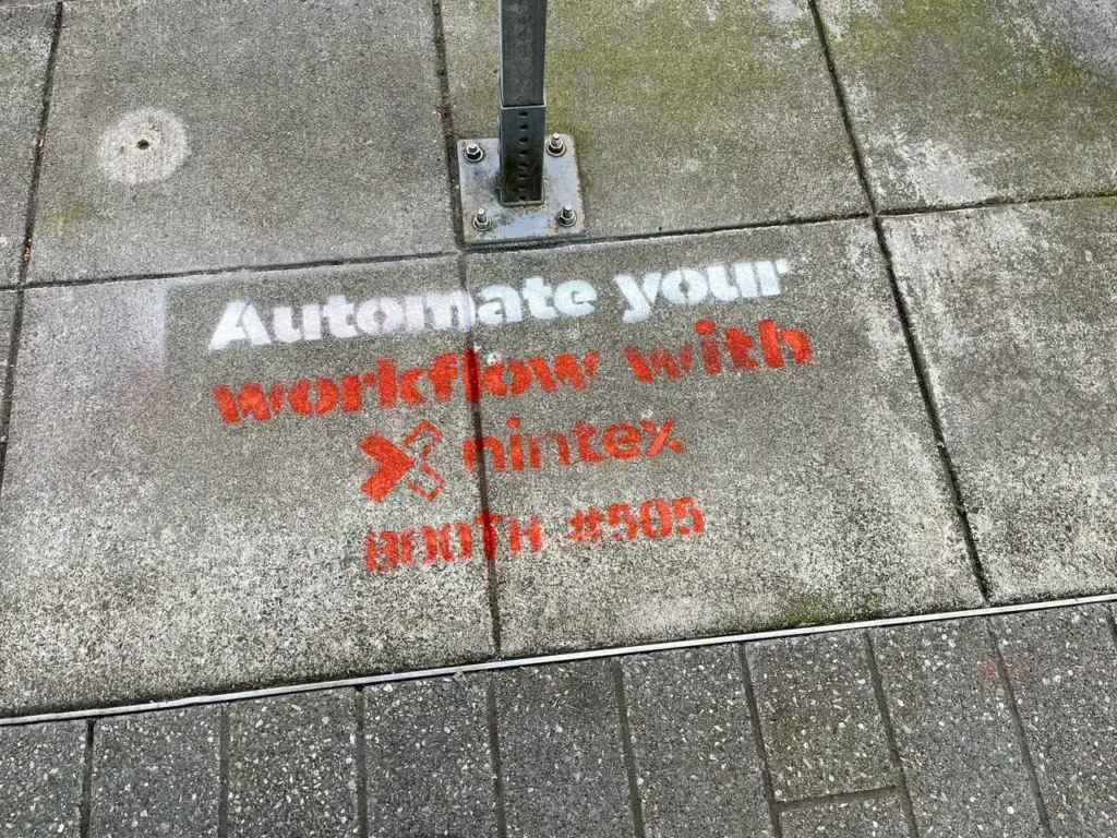 Sidewalk stencil advertising promoting workflow automation with Nintex, featuring the phrase "Automate your workflow with Nintex" and a hashtag.