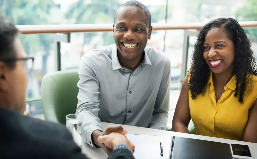 Smiling man and woman shaking hands in a business meeting, representing collaboration and partnership in marketing strategies.