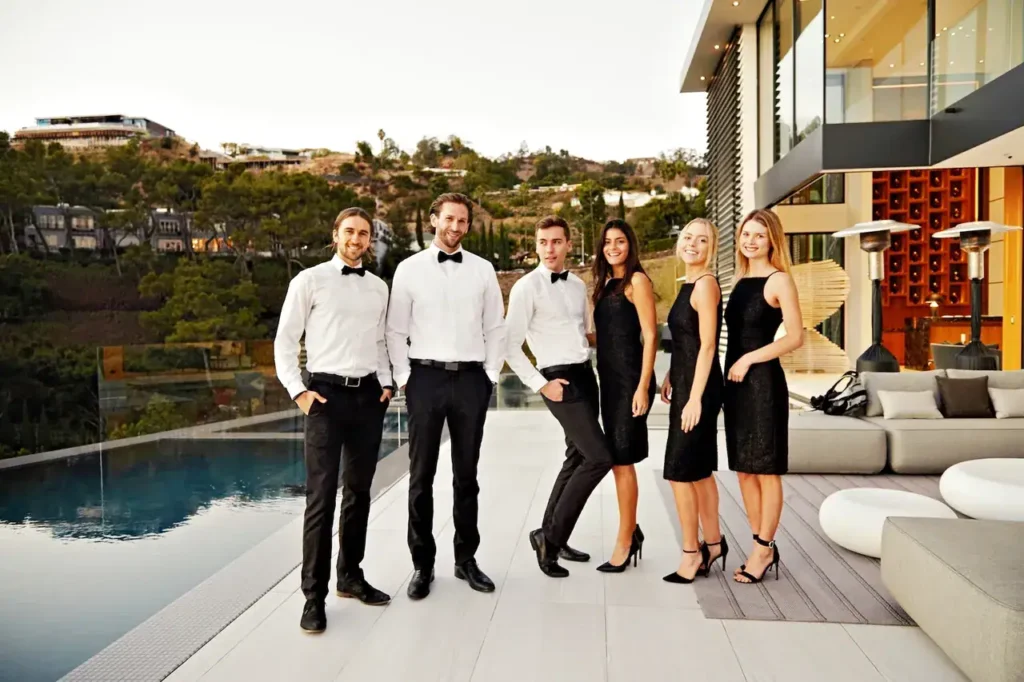 Group of six professionally dressed event staff in formal attire, standing by a luxury poolside setting, showcasing event staffing services for upscale events.