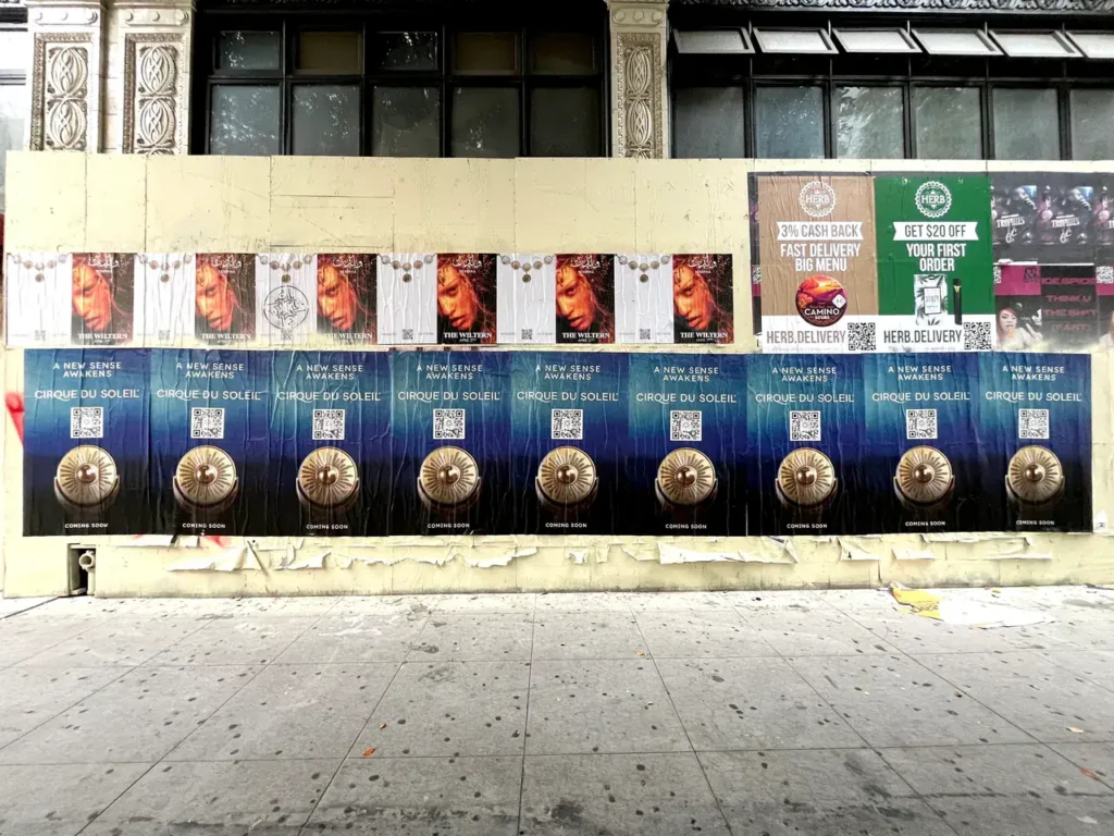 Wall covered with street advertising posters for Cirque du Soleil, featuring vibrant imagery and QR codes, showcasing guerrilla marketing techniques in urban environments.