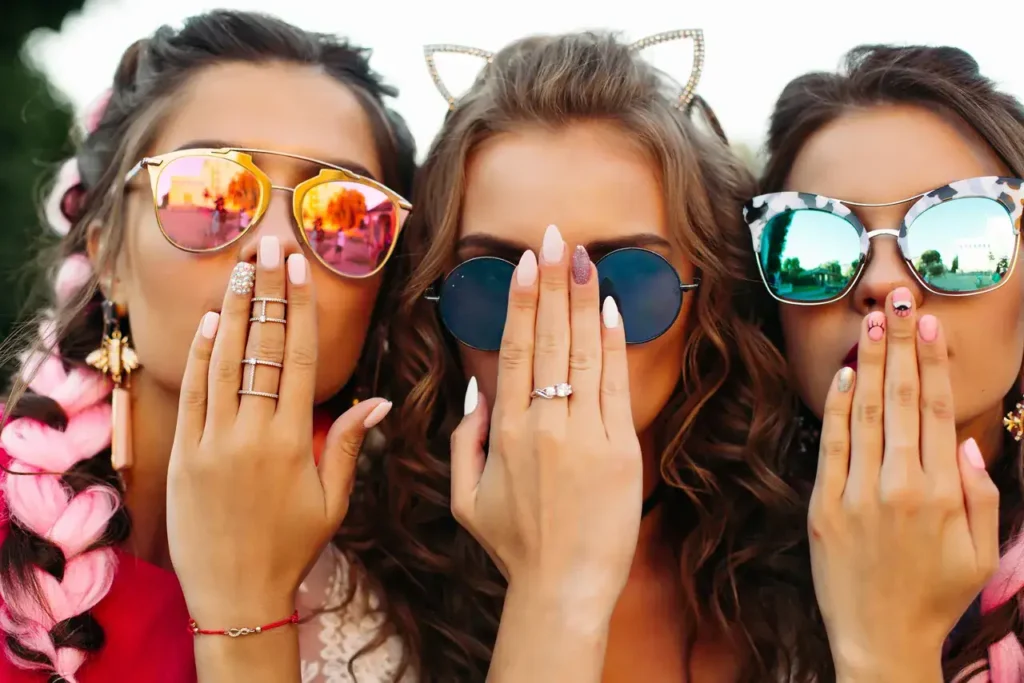 Three women wearing stylish sunglasses and playful expressions, covering their mouths with their hands, showcasing a fun and trendy atmosphere, relevant to brand ambassador marketing and engagement strategies.