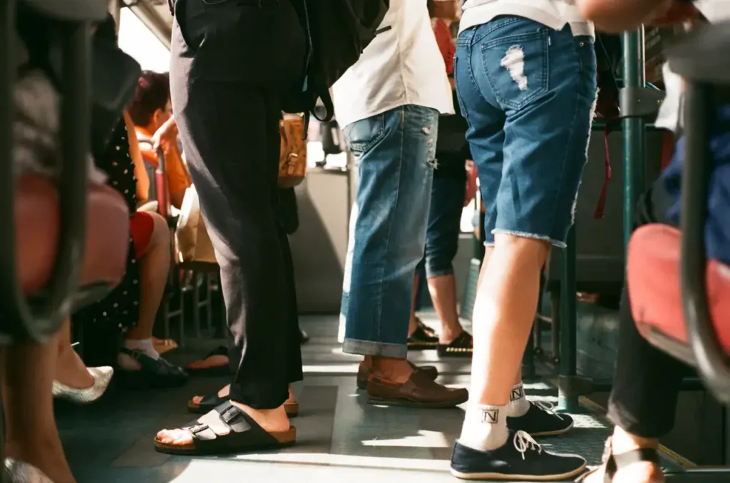 People standing in a public transport setting, showcasing diverse footwear and casual attire, emphasizing commuter lifestyle.