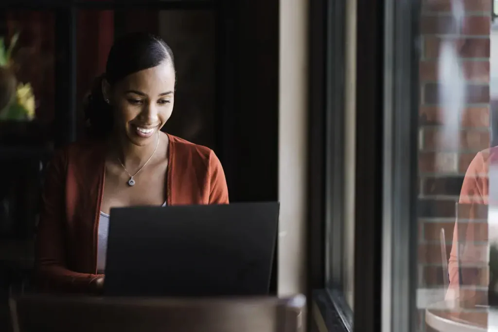 Smiling woman using laptop in a cafe, representing effective event planning and staffing solutions for American Guerrilla Marketing.