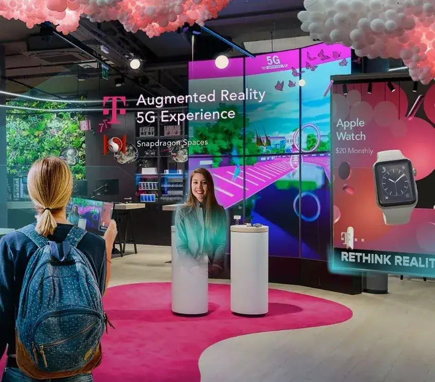 Augmented reality 5G experience display with a woman in a holographic presentation, showcasing Snapdragon Spaces and Apple Watch advertisements in a modern retail environment.
