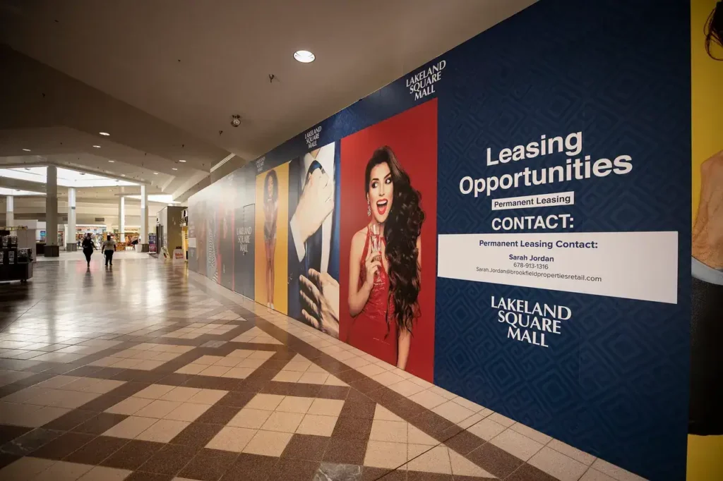 Wall advertisement promoting leasing opportunities at Lakeland Square Mall, featuring vibrant images of models and contact information for leasing inquiries.