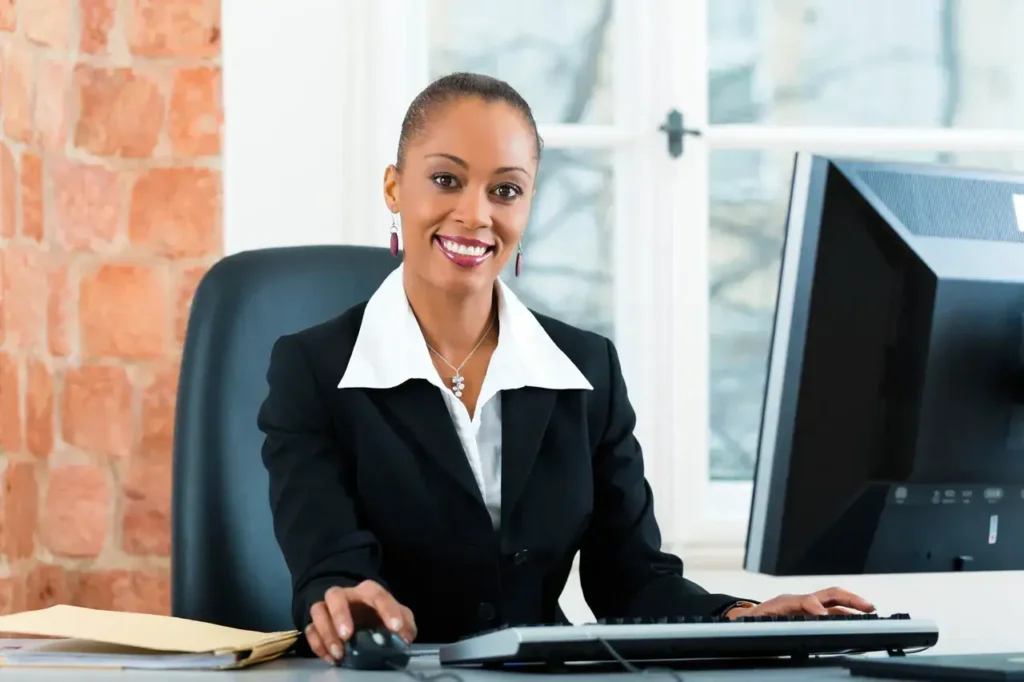 Smiling businesswoman in a professional suit at a desk with a computer, symbolizing effective marketing strategies and office productivity.