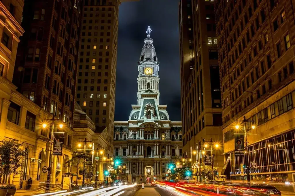 Philadelphia cityscape at night featuring the illuminated Philadelphia City Hall clock tower, surrounded by tall buildings and light trails from passing cars, relevant to billboard advertising in Philadelphia.