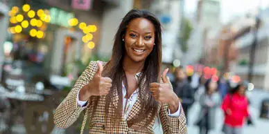 Smiling woman in a stylish outfit giving thumbs up in an urban setting, representing brand ambassador services and positive engagement for American Guerrilla Marketing.