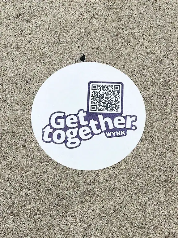 Sidewalk decal featuring the text "Get together" and a QR code, promoting engagement for WYNK, on a concrete surface.