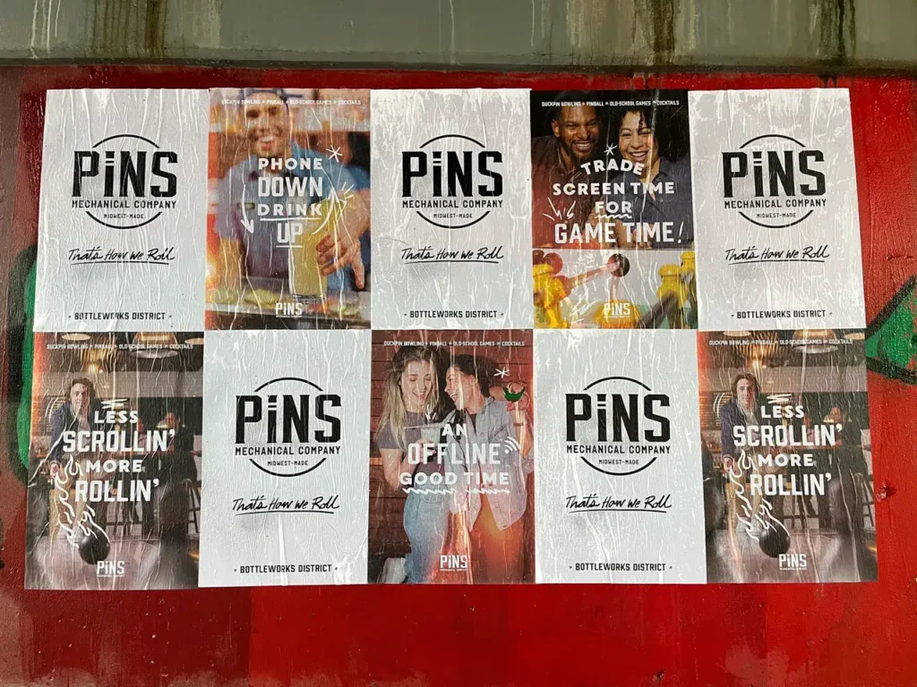 Advertising posters for PiNS Mechanical Company promoting social engagement, featuring slogans like "Phone Down Drink Up" and "Trade Screen Time for Game Time," set in the Bottleworks District.