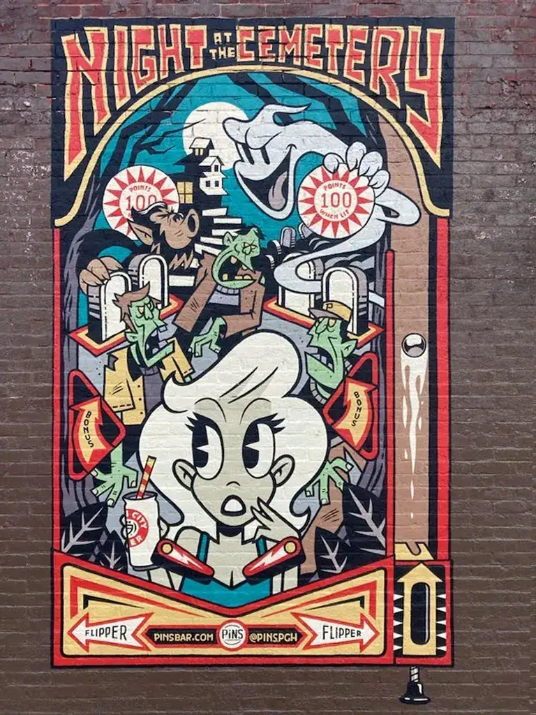 Colorful mural titled "Night at the Cemetery" featuring cartoonish characters, zombies, and playful imagery, promoting a themed event for bars and restaurants.