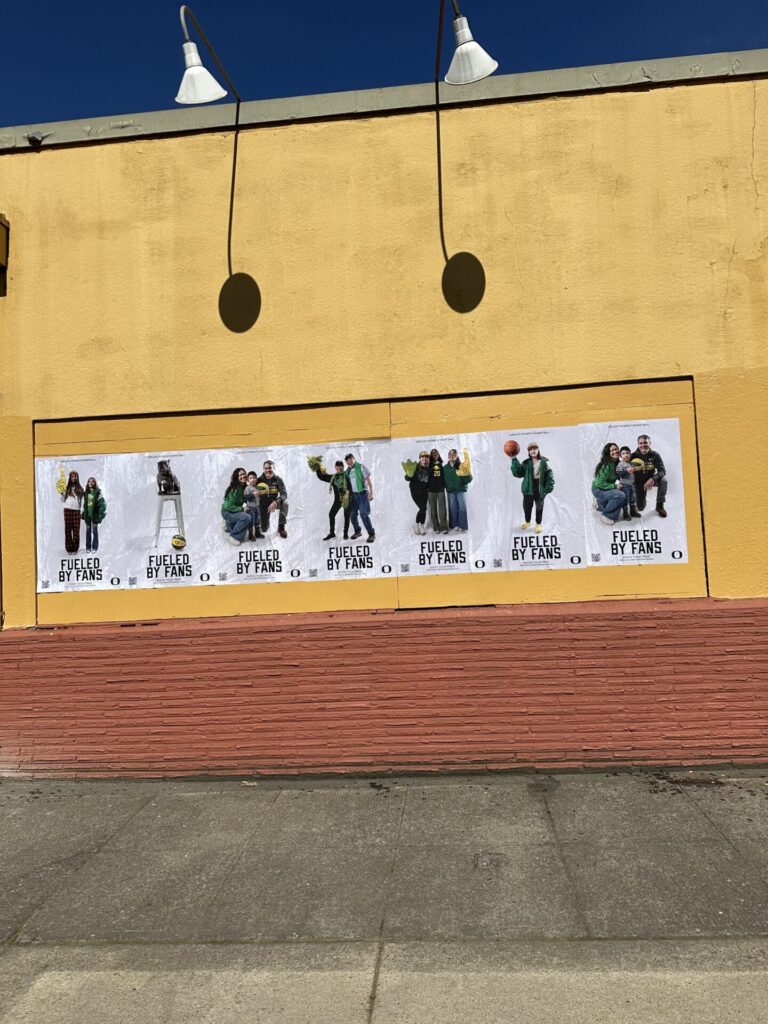 Wall display featuring multiple posters with the phrase "Fueled by Fans," showcasing diverse groups of people celebrating and promoting local brand engagement in advertising.