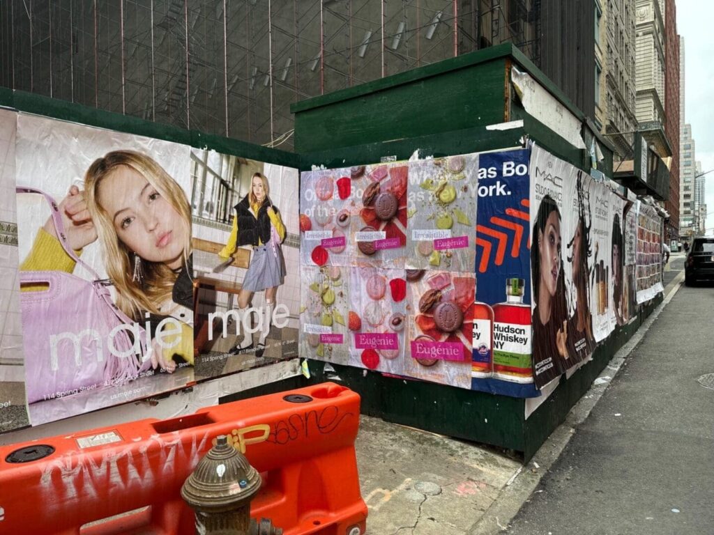 Street scene featuring various promotional posters and advertisements for beauty products and fashion brands, showcasing guerrilla marketing tactics in urban settings.