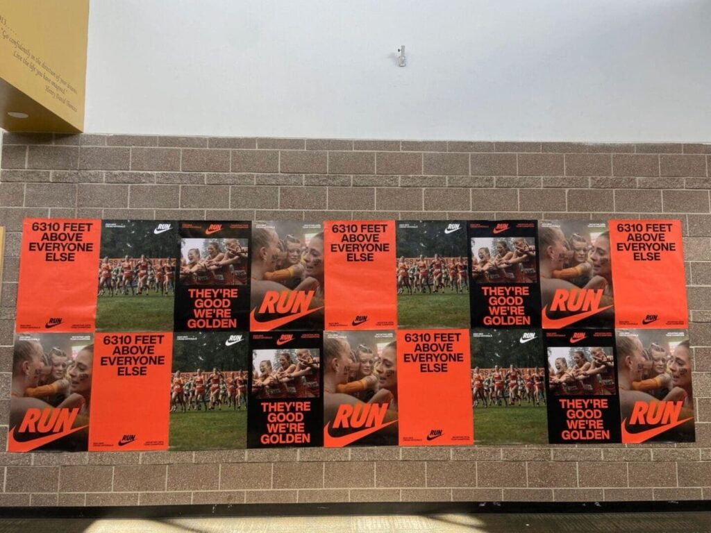 Advertising posters featuring Nike branding with motivational phrases like "RUN" and "6310 FEET ABOVE EVERYONE ELSE," displayed on a brick wall, promoting athleticism and brand visibility.