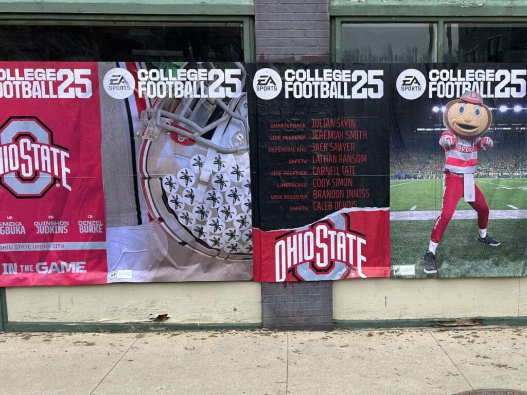 Ohio State University football promotional banners featuring team logo, player names, and imagery related to EA Sports College Football 25, displayed on a storefront.