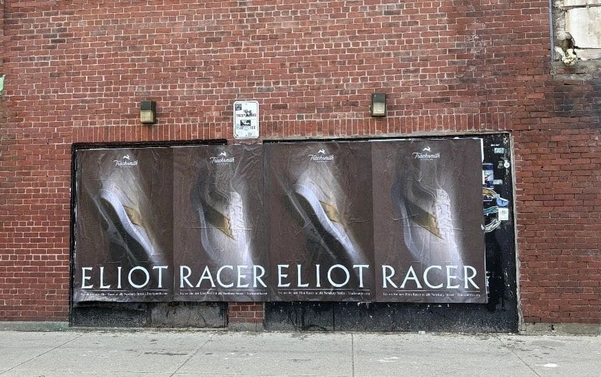 Posters promoting "Eliot Racer" on a brick wall, showcasing guerrilla marketing techniques for engaging audiences in urban environments.