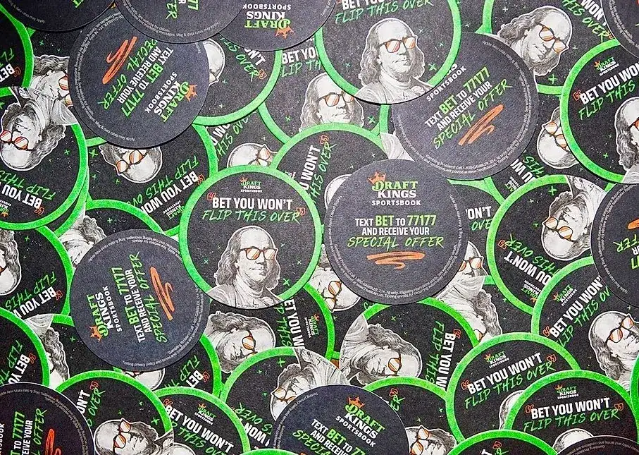 Branded beer coasters featuring DraftKings Sportsbook promotions, including text "Bet You Won't Flip This Over" and a special offer invitation, highlighting local advertising strategies for bars and restaurants.