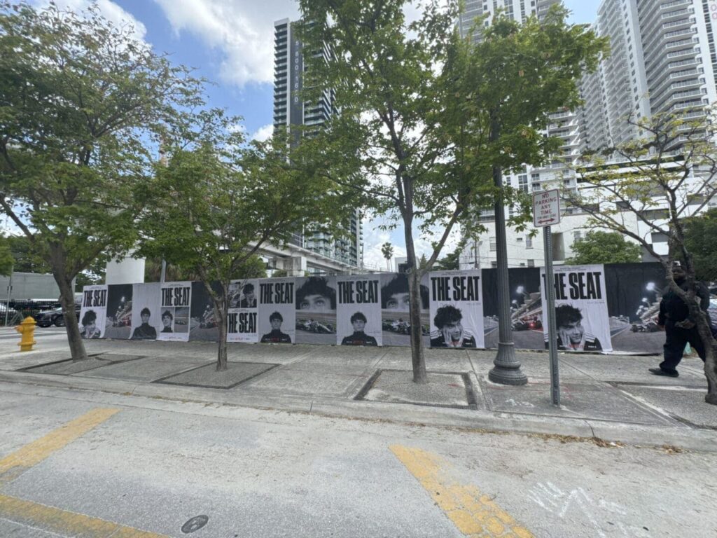 Large mural featuring black-and-white portraits with the text "THE SEAT," surrounded by trees and urban buildings, showcasing guerrilla marketing in a city setting.