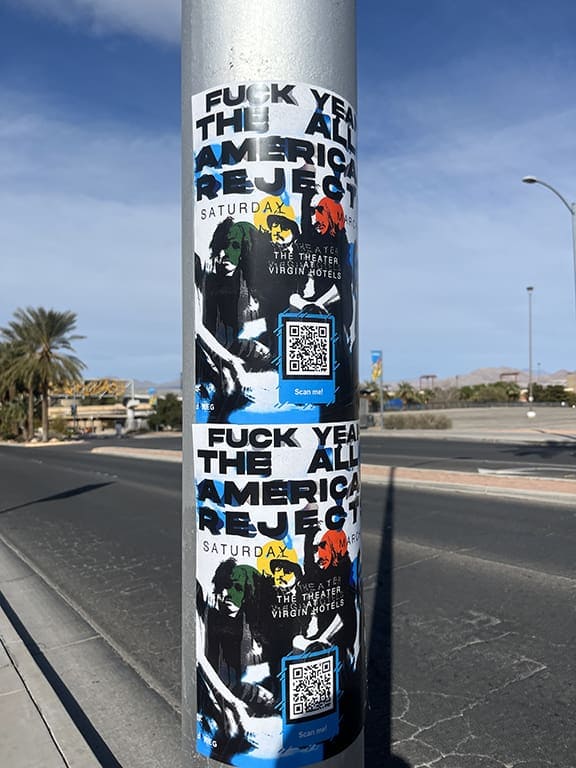 Wild wheat paste poster advertising The All-American Rejects concert, featuring colorful graphics and a QR code for event details, displayed on a street pole.