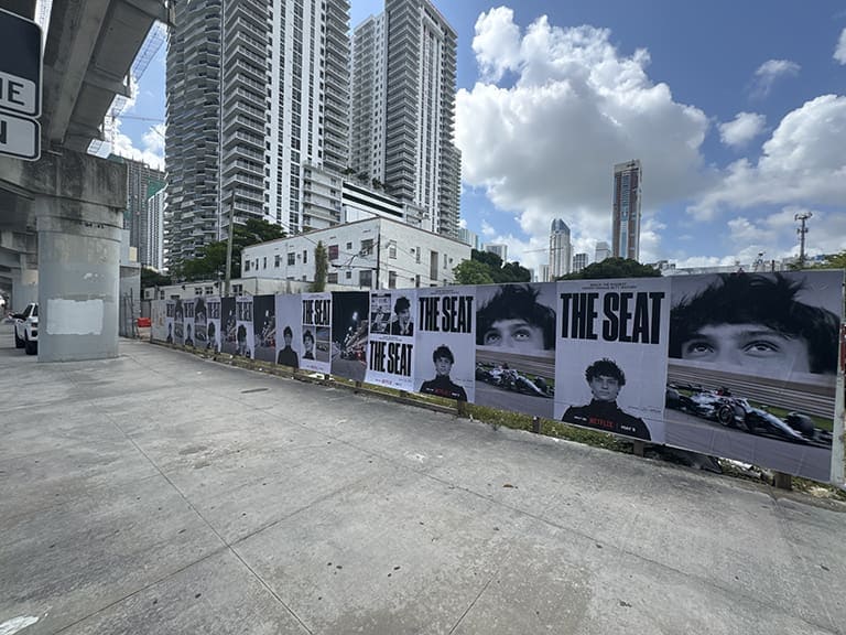 Billboard display featuring multiple large images of individuals with the text "THE SEAT," set against an urban backdrop, emphasizing guerrilla marketing strategies in experiential advertising.