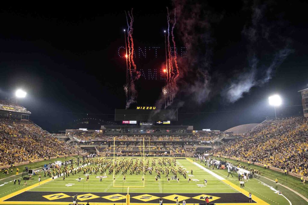 Fireworks display above Mizzou stadium during a nighttime event, with fans celebrating on the field and the crowd in the stands, emphasizing the excitement of experiential marketing in sports.