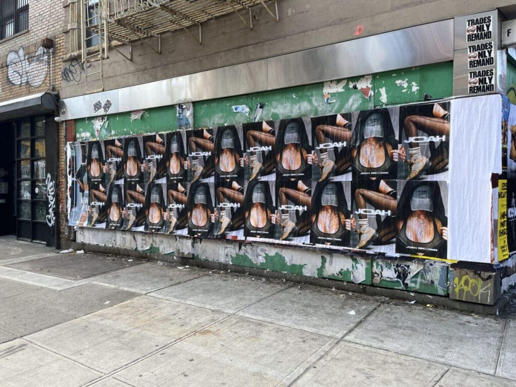 Wall covered in guerrilla marketing posters for JCOAH, featuring artistic imagery and bold branding, showcasing innovative advertising strategies relevant to experiential marketing discussions.