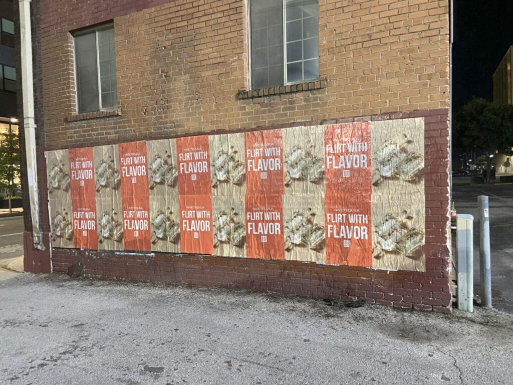 Posters on brick wall promoting "Flirt with Flavor" tequila campaign, showcasing guerrilla marketing strategy in urban setting.