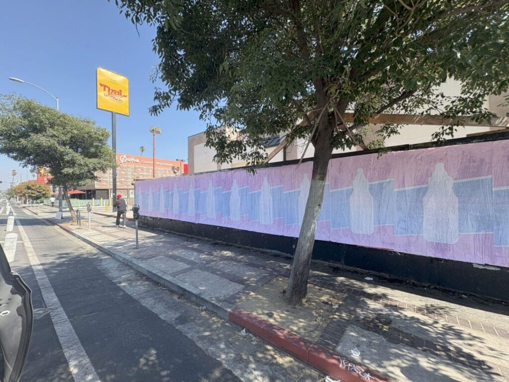 Mural on a building wall featuring abstract figures in pastel colors, with trees and a street view, highlighting guerrilla marketing creativity in urban environments.