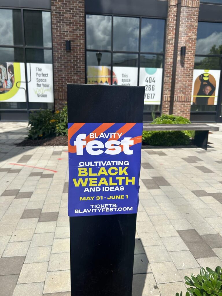 Signpost displaying "BLAVITY fest" promoting an event focused on cultivating Black wealth and ideas, scheduled for May 31 to June 1, with a website link for tickets.