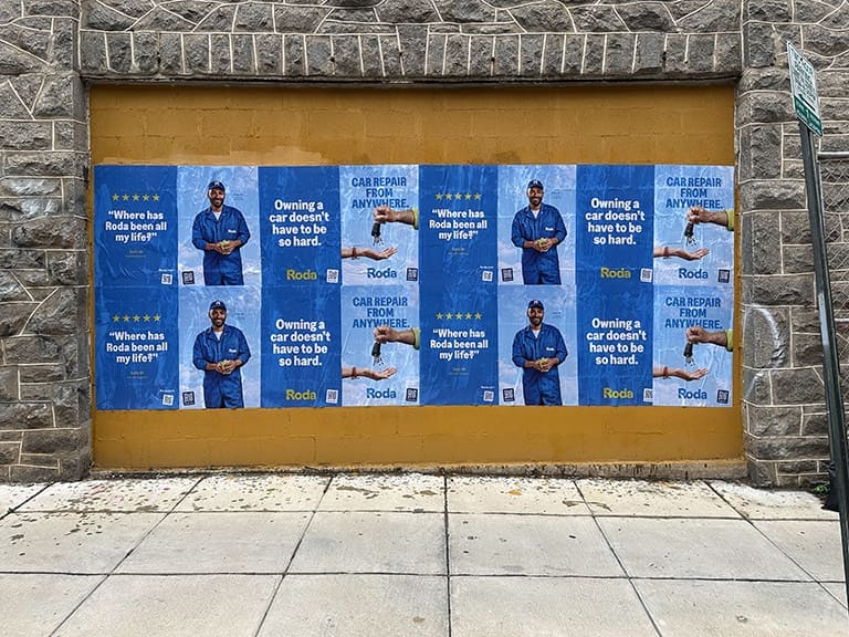 Wall covered with posters advertising car repair services, featuring a mechanic in blue overalls, slogans about car ownership, and the brand name "Roda," relevant to guerrilla marketing strategies targeting college students.